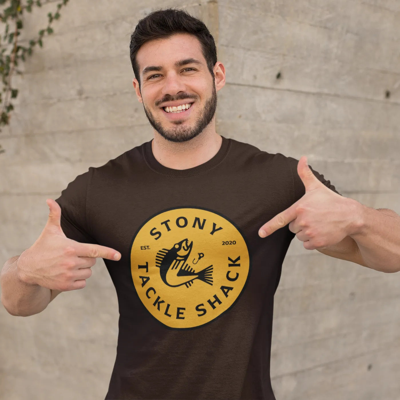 Man wearing a brown t-shirt with 'Stony Tackle Shack' logo, pointing at it.
