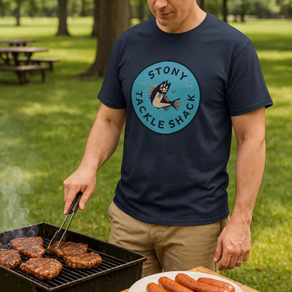Man grilling hot dogs and hamburgers wearing a navy blue t-shirt with 'Stony Tackle Shack' logo.