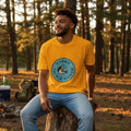 Man wearing a yellow t-shirt with a logo sitting on a log in a forest.