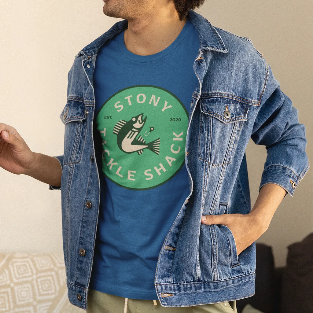 Man wearing a blue denim jacket over a blue t-shirt with a green logo, standing in a casual indoor setting.