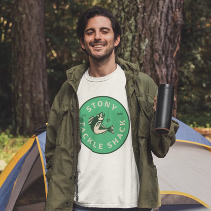Man standing in front of a tent wearing a white t-shirt with a green logo, surrounded by trees.