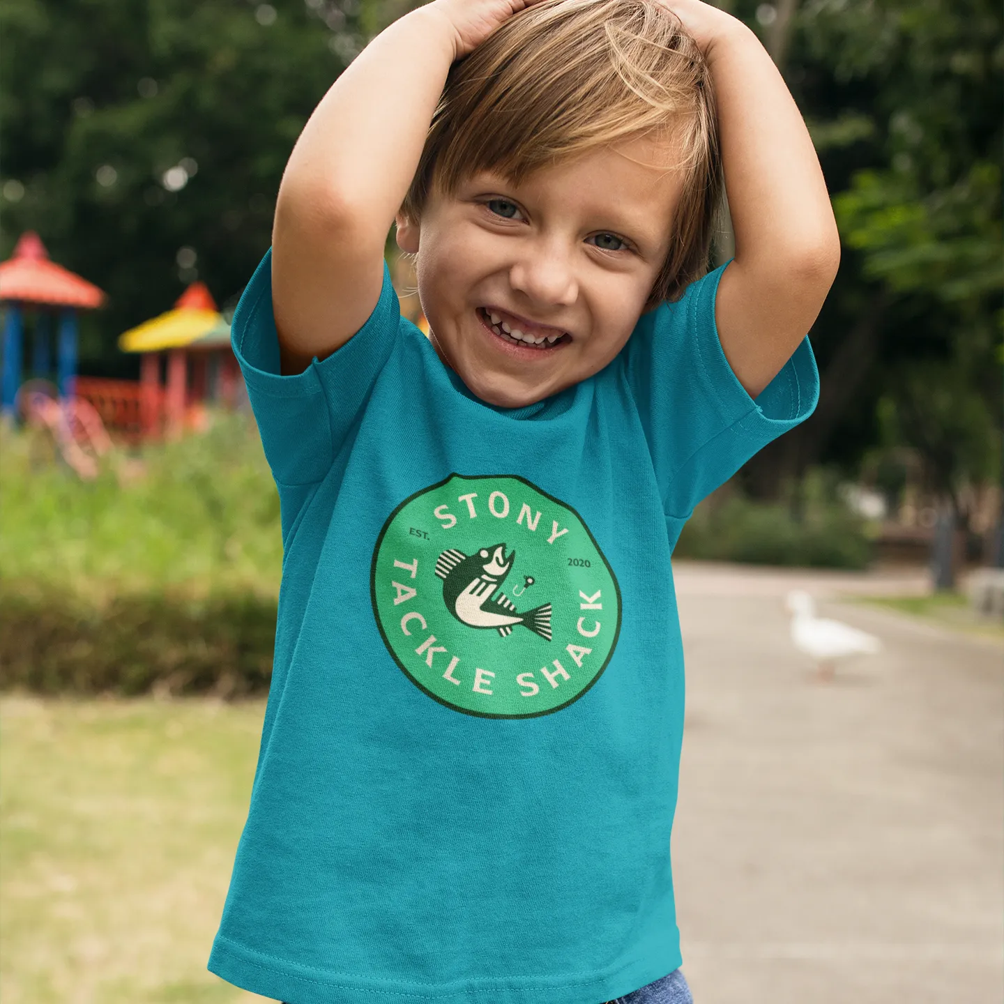 Child wearing a blue t-shirt with a green logo in an outdoor setting