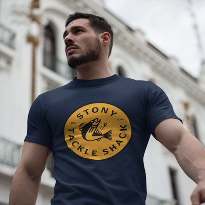 Man wearing a navy blue t-shirt with yellow 'Stony Tackle Shack' logo in front of a building.
