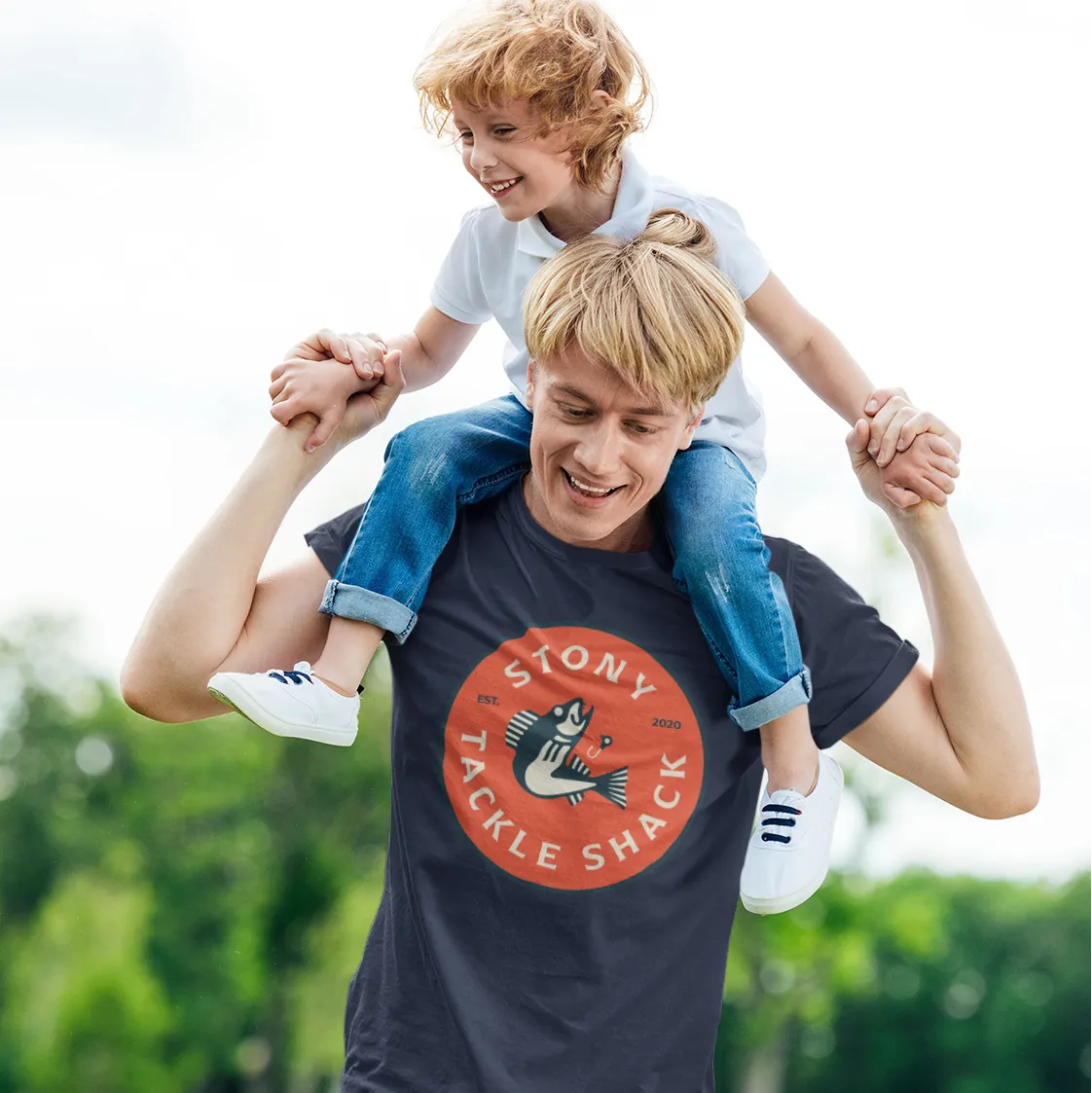 Man carrying a child on his shoulders with a navy 'Stony Tackle Shack' t-shirt with red logo.