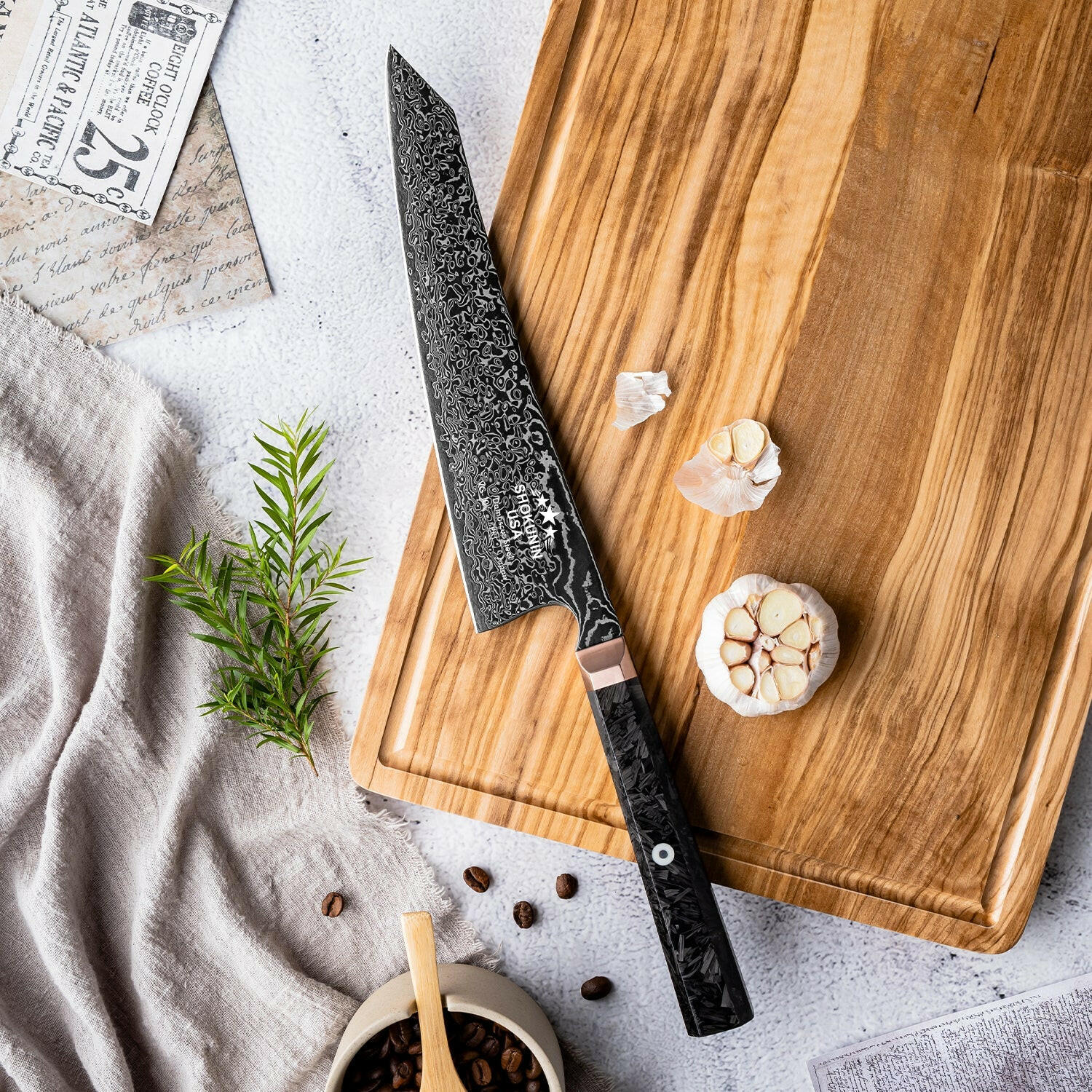 Decorative chef's knife on a wooden cutting board with garlic and herbs on a light gray surface.