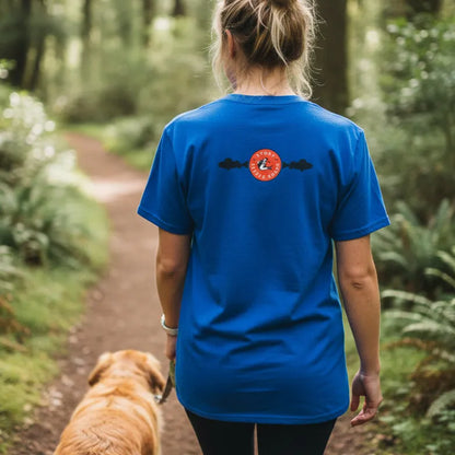 Person wearing a blue t-shirt with a red logo walking a dog on a forest path