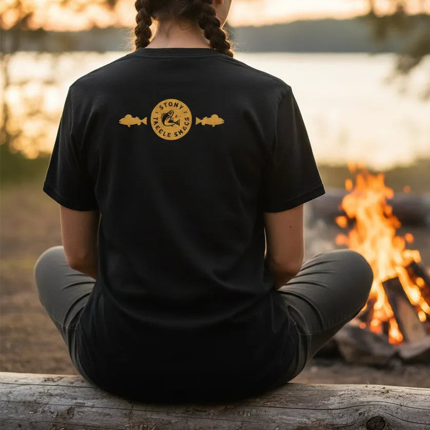  Girl with Black t-shirt with a yellow logo on the back sitting by campfire