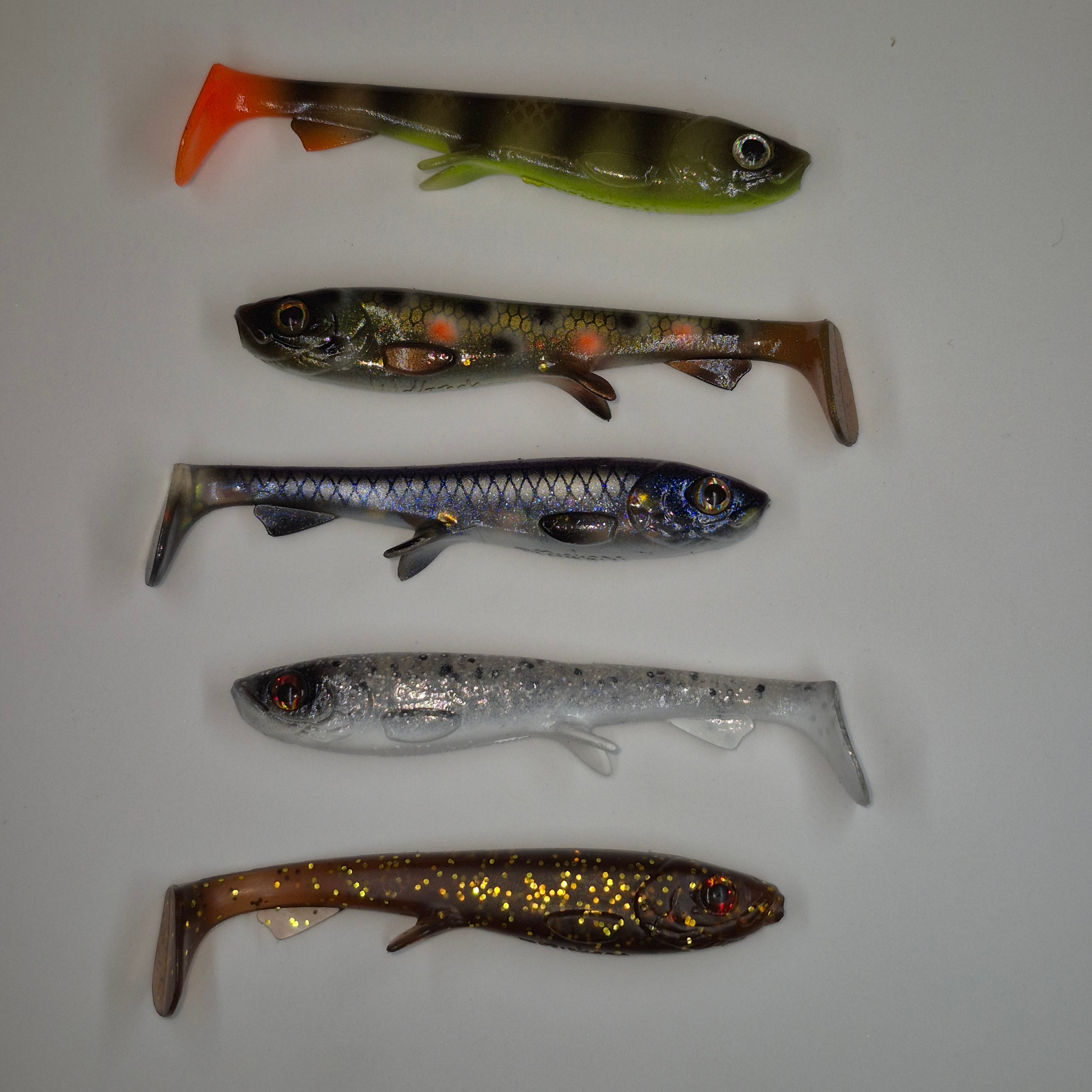 Five soft plastic fishing lures shaped like small fish, arranged vertically on a plain light background. The lures vary in color and pattern, including olive green, gray-brown, blue-silver, silver, and bronze-gold.