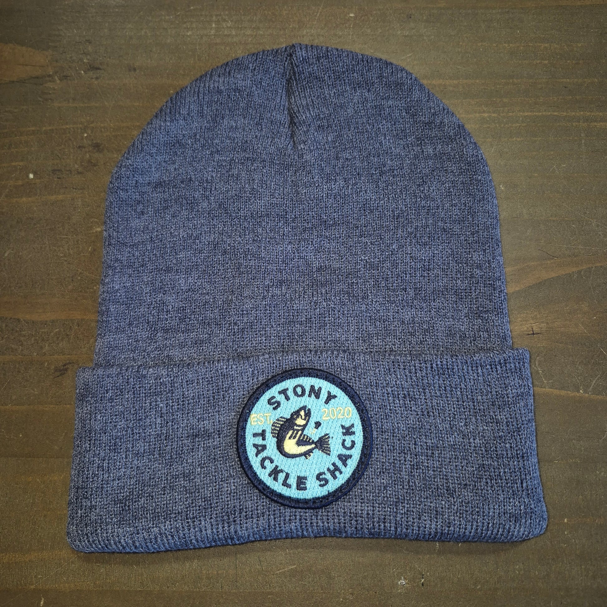 Blue knit beanie with a logo on a wooden surface