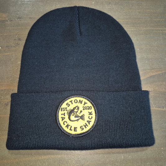 Black knit beanie with a yellow logo patch on a wooden surface