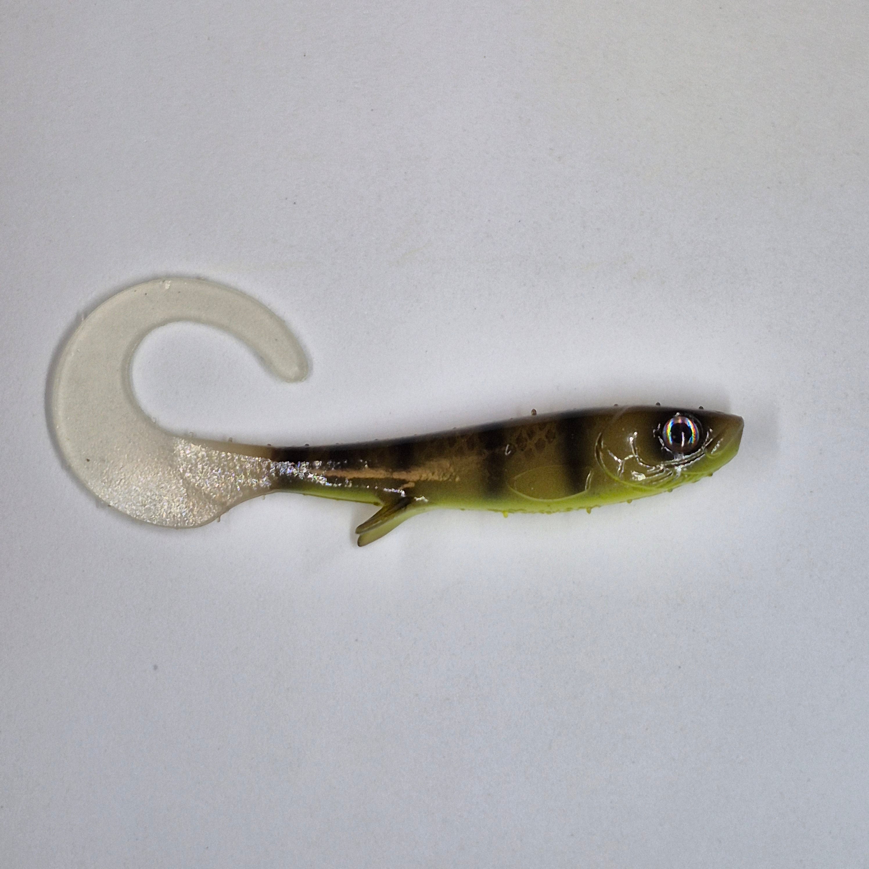 A soft plastic fishing lure shaped like a small fish with a curved tail, shown on a plain light background. The lure has a translucent clear tail, a yellow-green body, and dark vertical stripes.