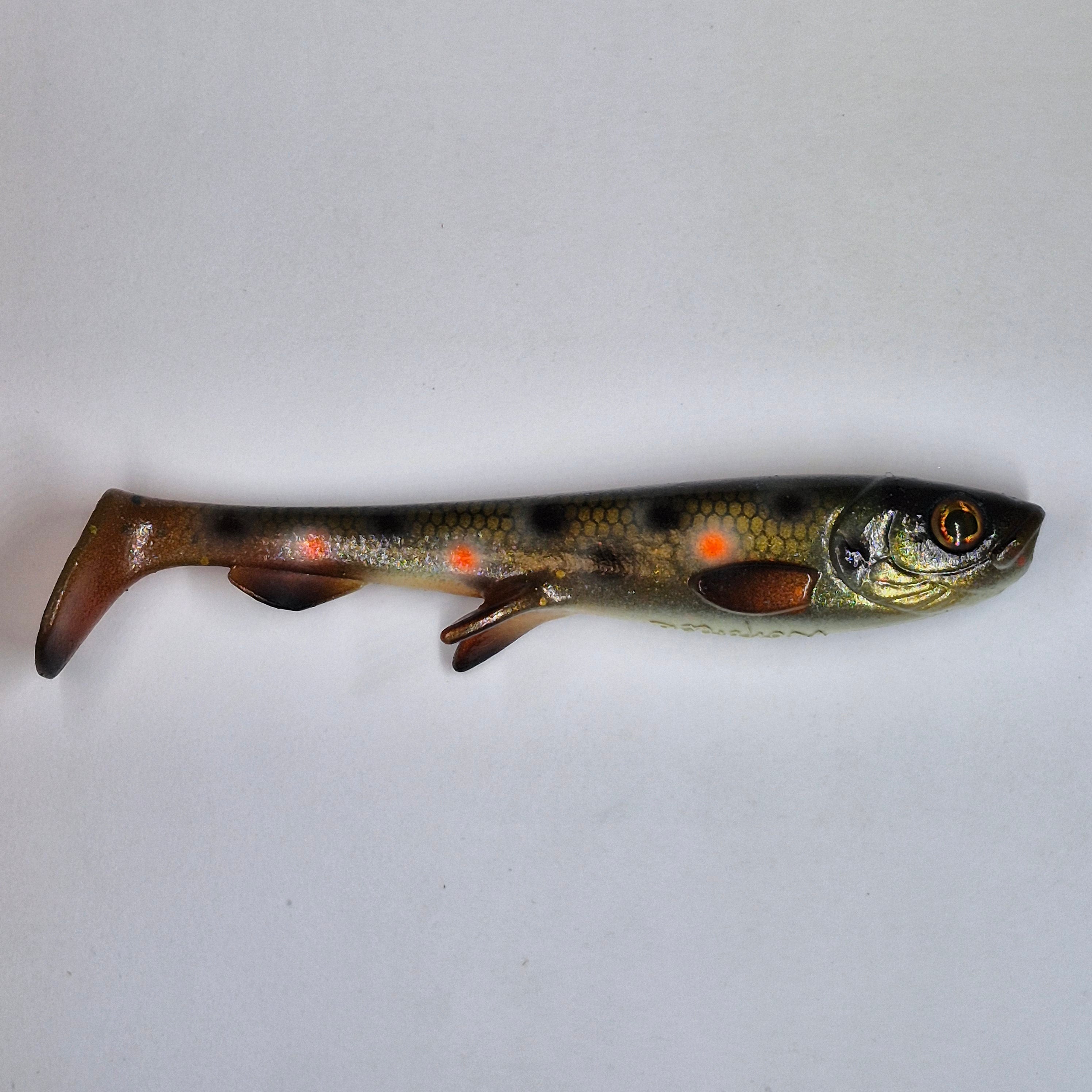 A realistic soft plastic fishing lure shaped like a small trout, featuring a mottled brown and gold body with orange spots and a detailed eye, shown on a plain light gray background.