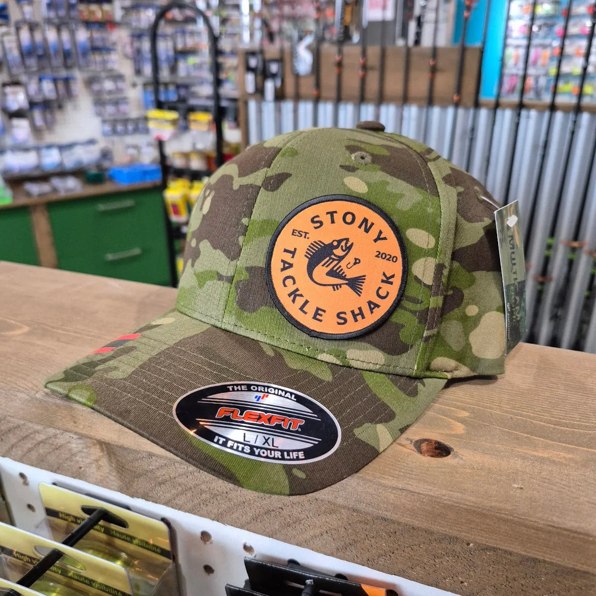 Camouflage hat with Stony Tackle Shack logo on a wooden surface.