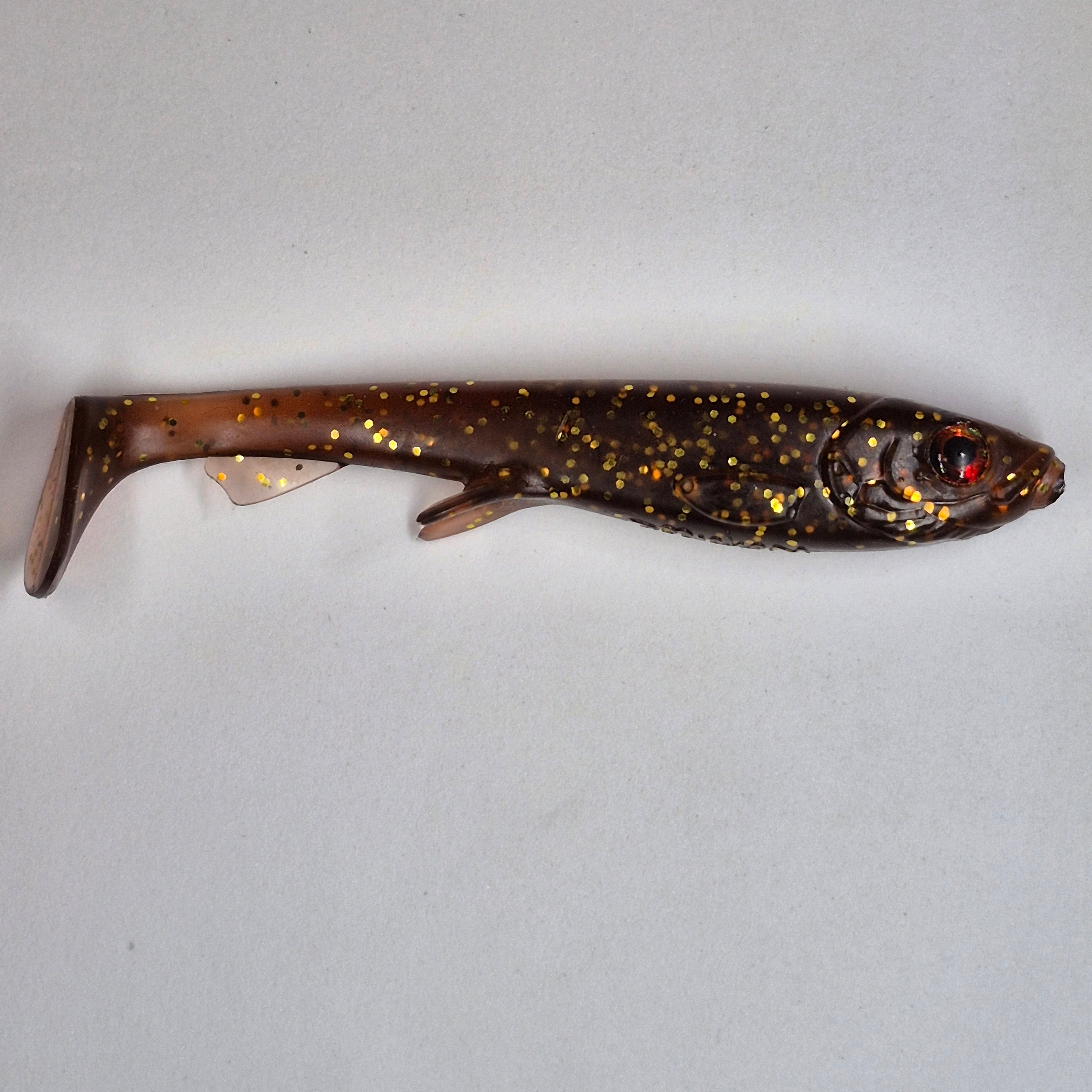 A realistic soft plastic fishing lure shaped like a small fish, featuring a dark brown body with gold glitter spots and a red eye, laid flat on a light gray background.