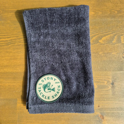 Black hand towel with Tan/Green Logo on wood background