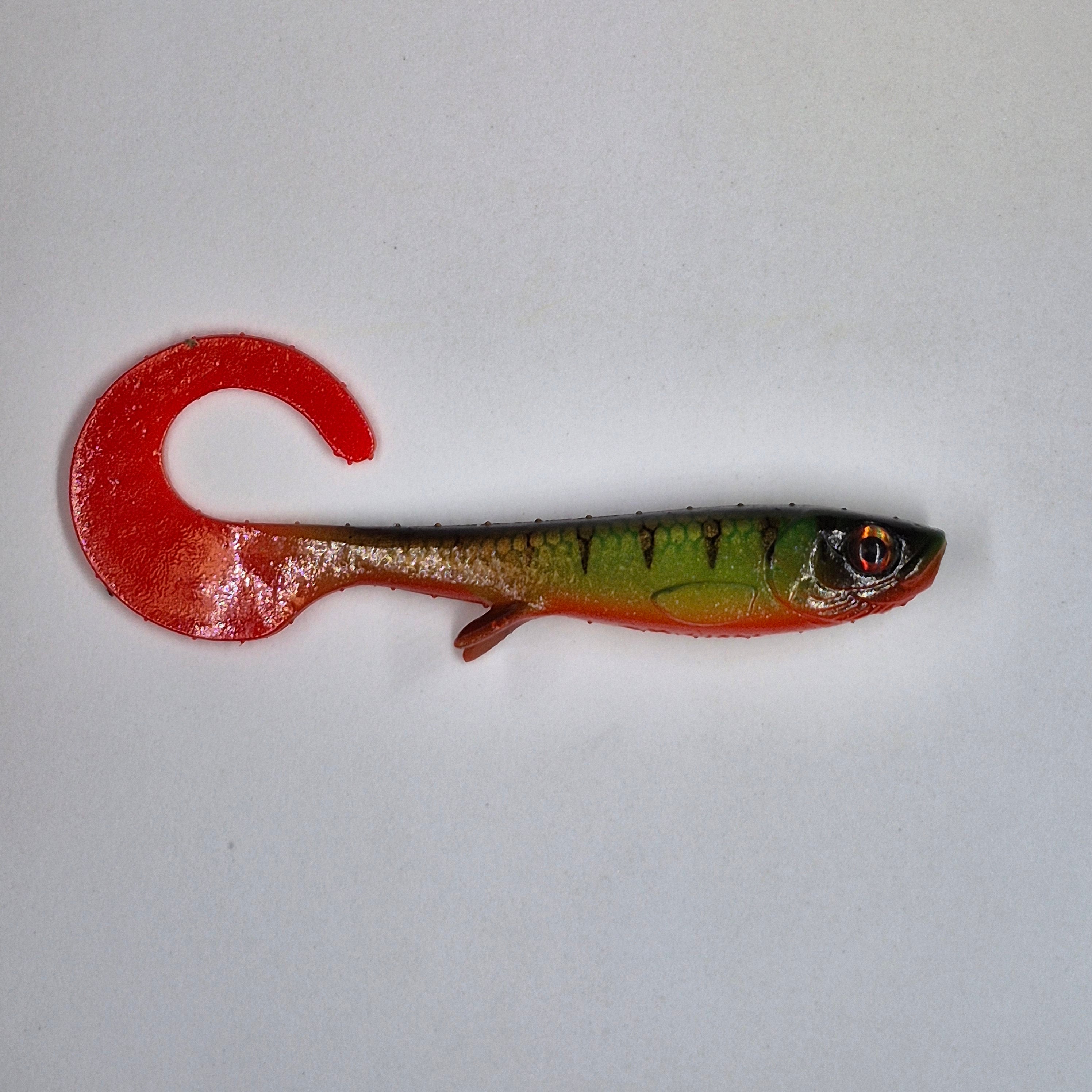 A soft plastic fishing lure shaped like a small fish, featuring a bright red tail and body gradient transitioning to green on the upper half, with a realistic eye detail, shown on a plain light gray background.